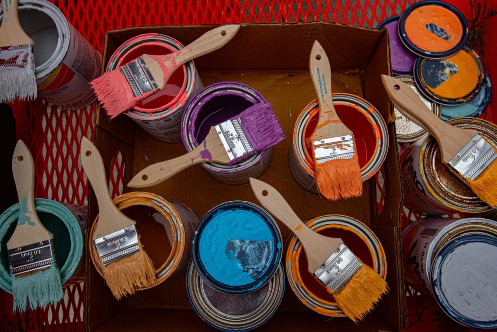 Picture of multi colored paint cans, each with dipped brushes on top.